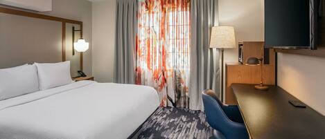 Une chambre d’hôtel avec un grand lit, un bureau, une chaise, une télévision et une fenêtre avec des rideaux.