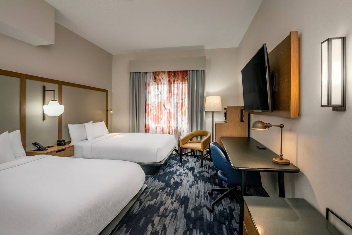Habitación de hotel con dos camas, un escritorio, una silla, un televisor y una ventana con cortinas.