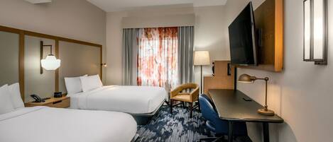 A hotel room with two beds, a desk, a chair, a TV, and a window with curtains.
