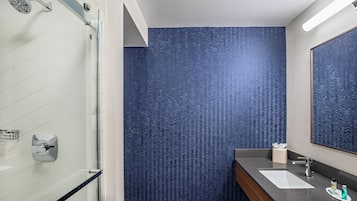 A bathroom with a glass shower enclosure, a white sink, and a mirror.