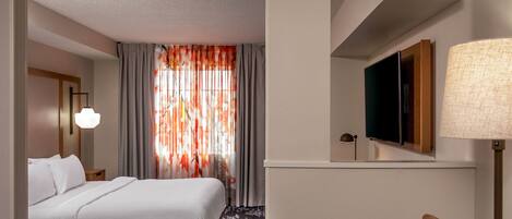 Habitación de hotel con cama, televisión montada en la pared, lámpara y ventana con cortinas.