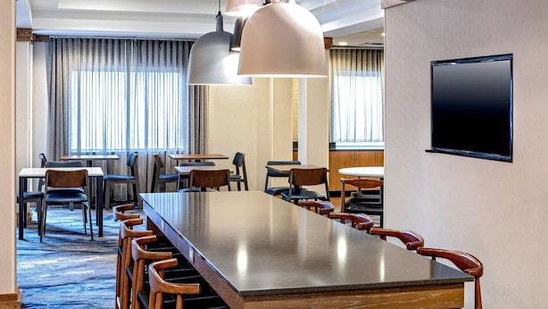 A hotel conference room with a long table, multiple chairs, pendant lights, a flat-screen TV, and large windows with curtains. - Fairfield Inn & Suites by Marriott Saratoga Malta (Ballston Spa)