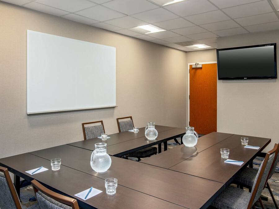 A conference room with a long table, chairs, a projector screen, and a flat-screen TV on the wall.