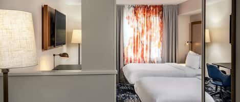A hotel room with two beds, a desk, a chair, a TV, and a lamp.