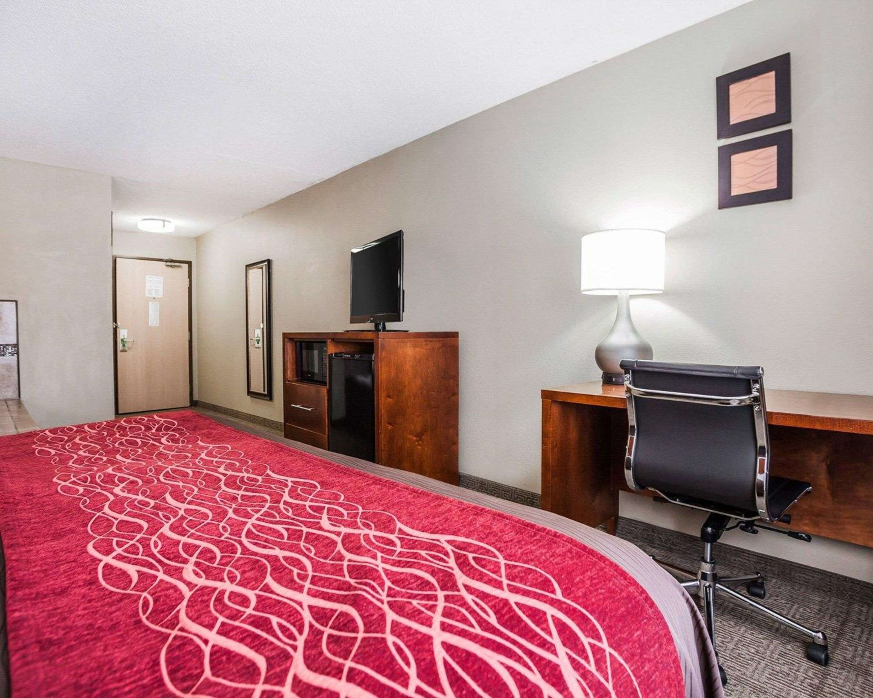 A hotel room with a large bed, a desk with a chair, a television, and a lamp.