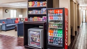 Un hall d’hôtel équipé d’un distributeur automatique rempli de collations et de boissons, d’un réfrigérateur contenant des boissons, et d’un espace détente avec un canapé et des fauteuils.