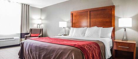 A hotel room with a large bed, two bedside tables with lamps, a chair, and a window with curtains.
