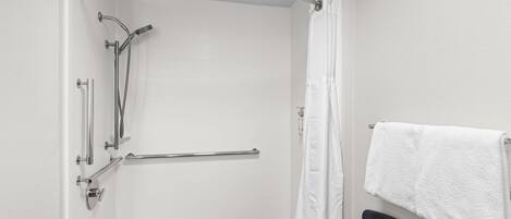 Baño con ducha, barras de apoyo, toallero y una silla.