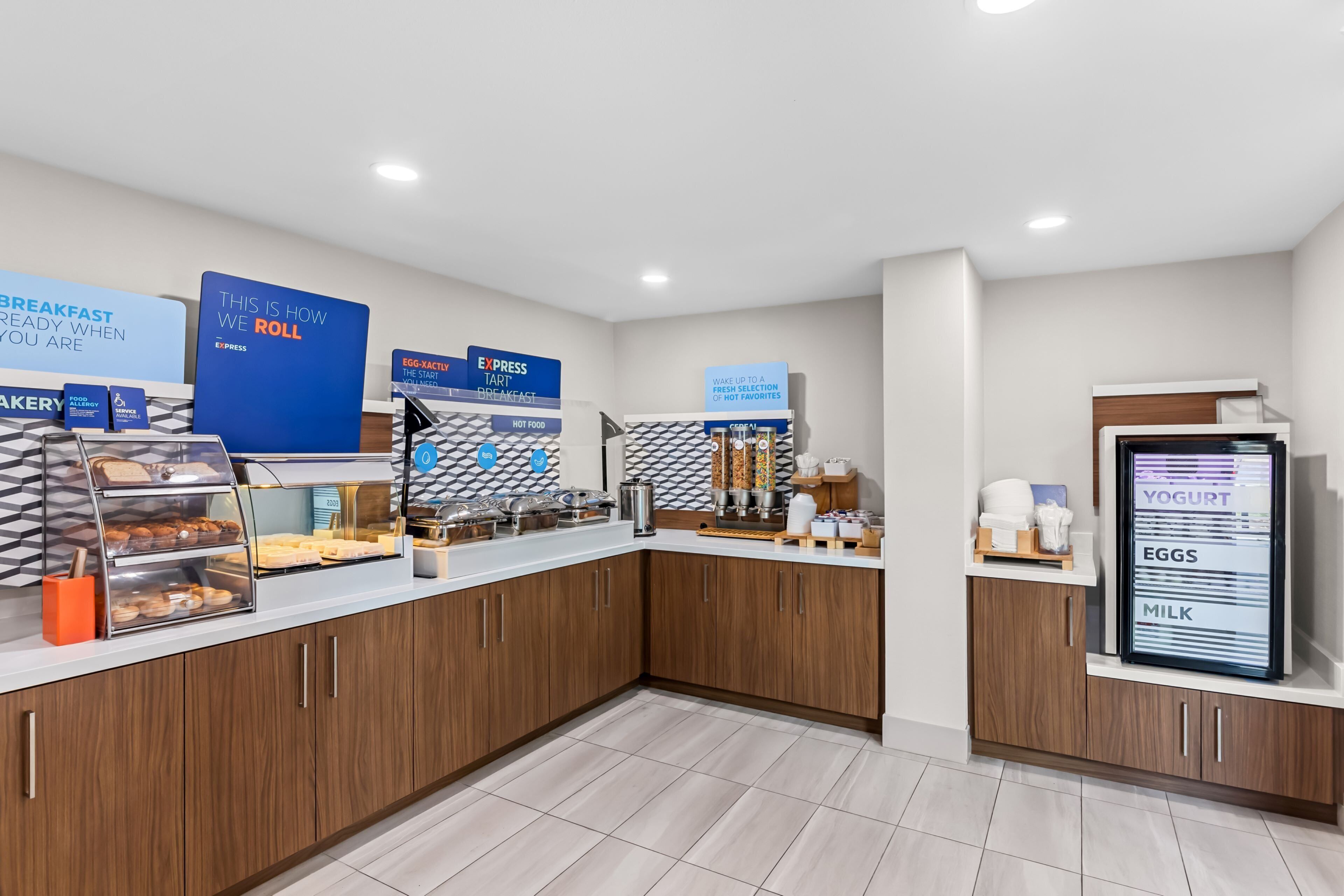 A breakfast bar with a variety of food options, including pastries, hot food, and a yogurt, eggs, and milk dispenser.