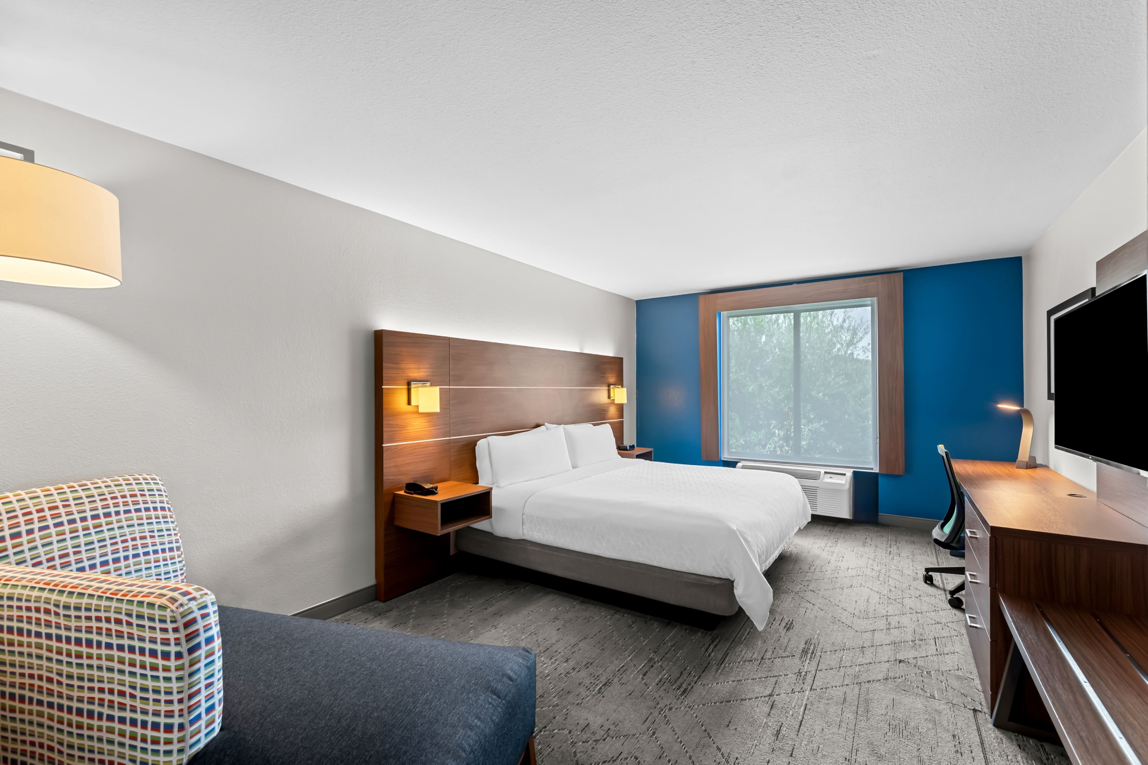 A hotel room with a bed, a desk, a TV, a chair, and a window.