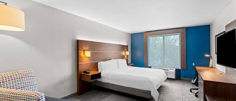 Una habitación de hotel con cama, escritorio, televisión, silla y ventana.