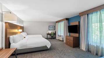 A hotel room with a bed, desk, TV, and curtains.