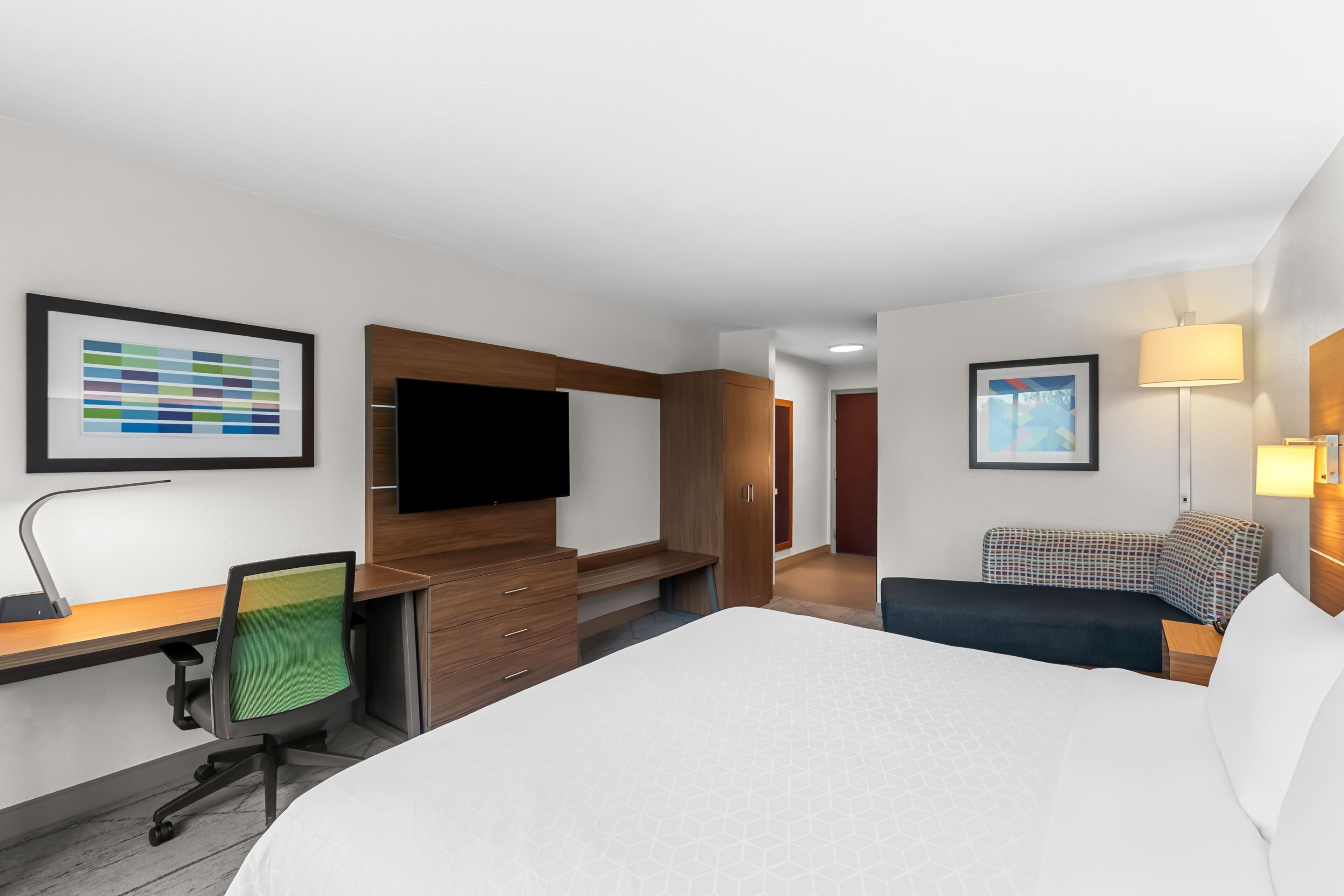A hotel room with a large bed, a desk with a chair, a TV, and a sofa.