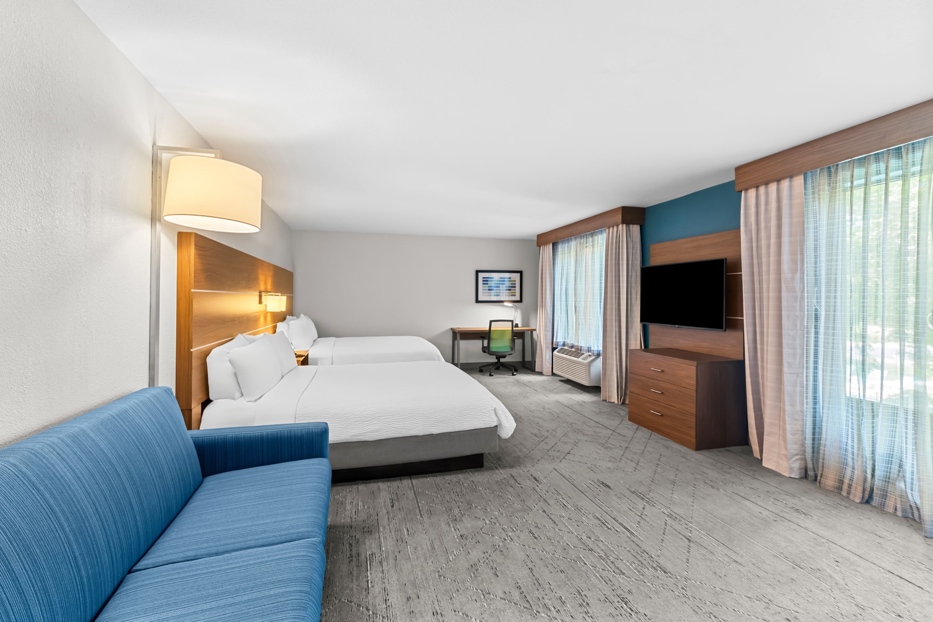 Habitación de hotel con una cama grande, un sofá azul, un escritorio con una silla, un televisor y una ventana con cortinas.