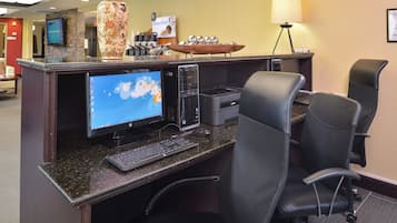 A hotel reception area with a desktop computer, two chairs, a coffee station, and a lamp.