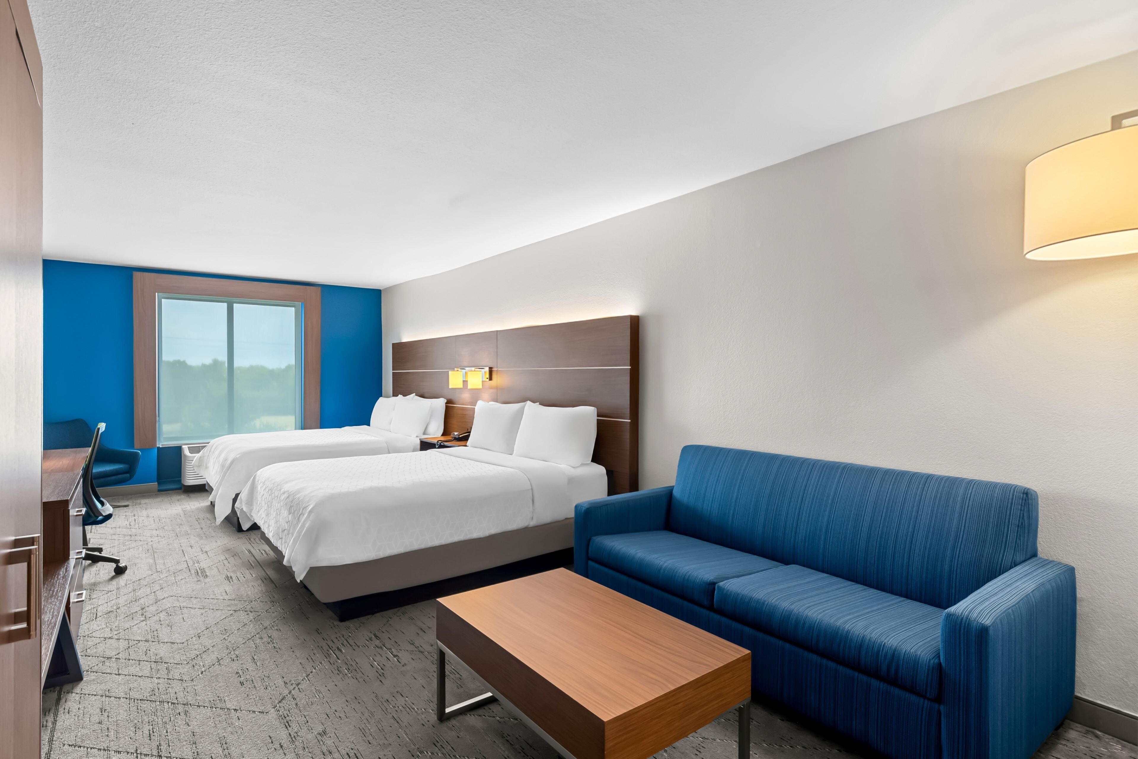 A hotel room with two beds, a blue sofa, a wooden coffee table, and a desk with a chair.