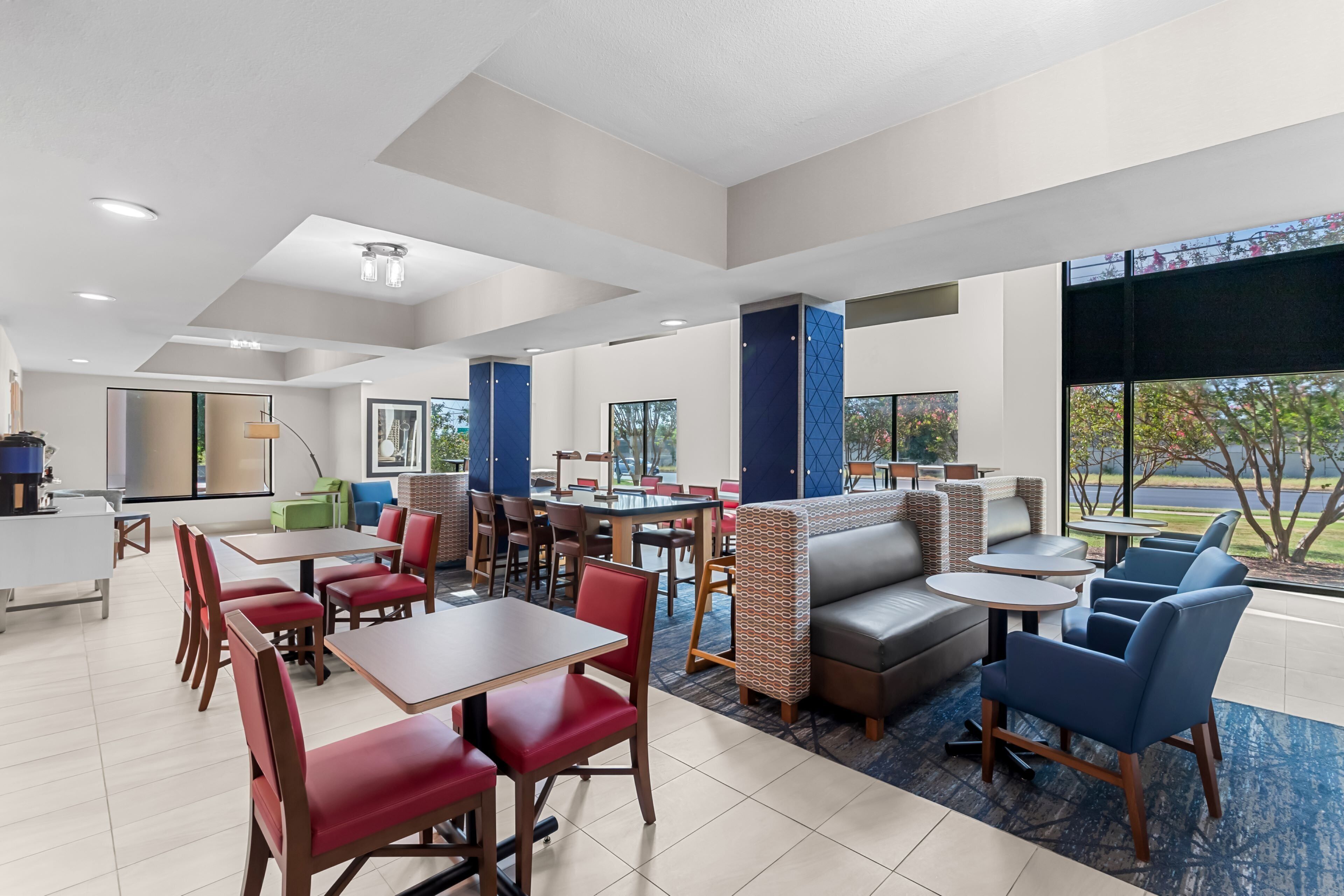 A modern hotel lobby with a mix of dining and seating areas, including tables, chairs, and a sofa.