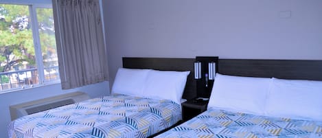 Habitación de hotel con dos camas, una ventana con cortinas, una mesita de noche y una mesita auxiliar.