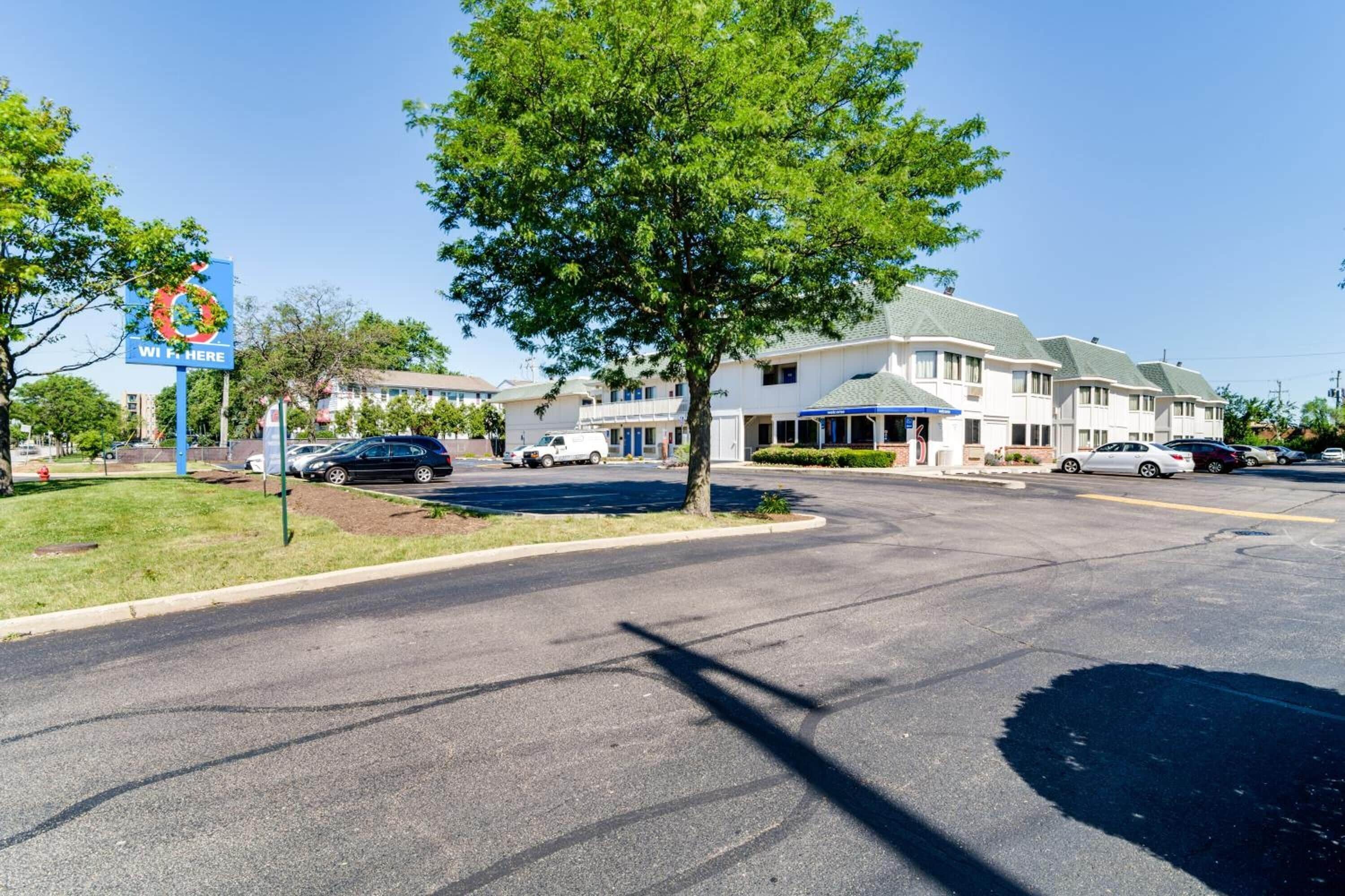 Un hôtel doté d’un grand parking, d’une enseigne ornée d’une guirlande et d’un arbre au premier plan.