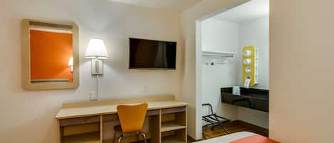 Habitación de hotel con cama, escritorio, silla, televisión, espejo y baño visible a través de una puerta abierta.