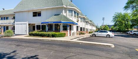 A hotel with a 'welcome' sign, a parking lot, and a building with a green roof.