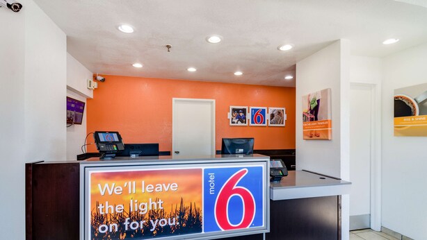 A motel reception desk with a large sign reading "We'll leave the light on for you" and the number 6. - Motel 6 Schiller Park, IL - Chicago O'Hare (Schiller Park)