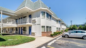 A two-story hotel with a balcony on the second floor, a parking lot, and a clear blue sky. - Motel 6 Schiller Park, IL - Chicago O'Hare (Schiller Park)
