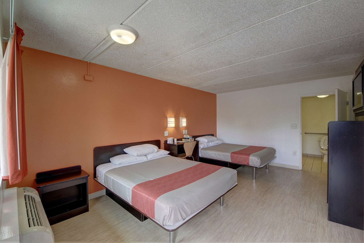 Une chambre d’hôtel avec deux lits, un bureau, une chaise et un radiateur.