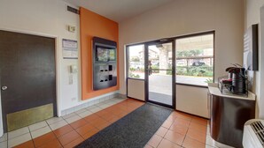 Un hall d’hôtel comprenant un comptoir d’accueil, un téléphone à pièces, un distributeur automatique et une vue sur l’extérieur à travers les portes vitrées.