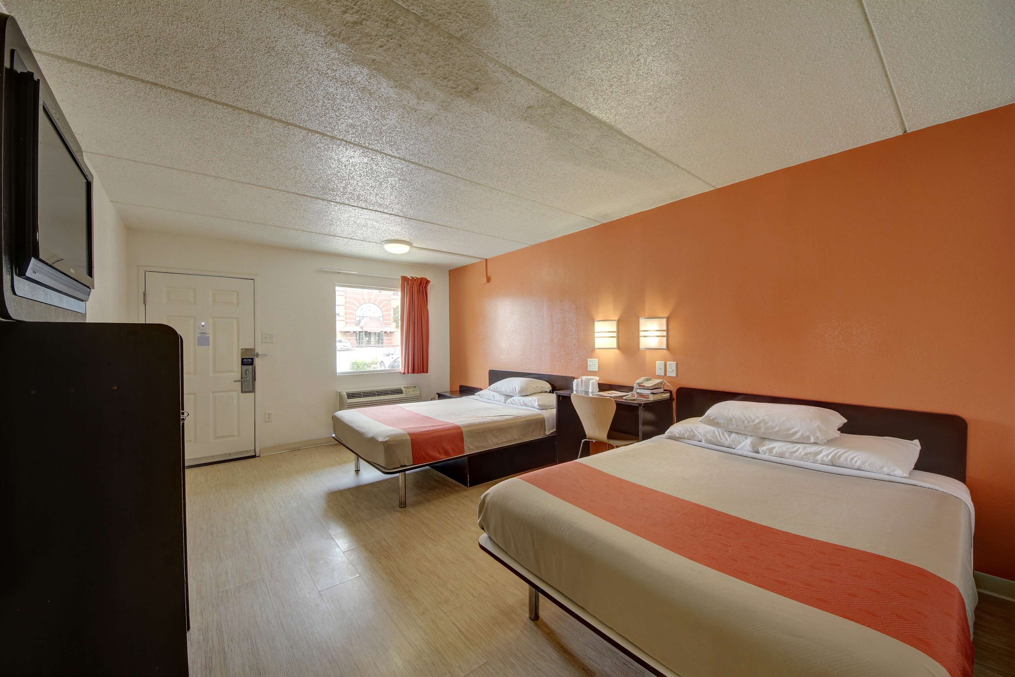A hotel room with two beds, a desk with a chair, a TV, and a window with curtains.