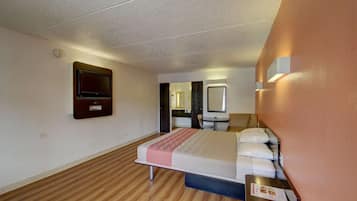 A hotel room with a bed, a desk, a chair, a television, and a mirror.