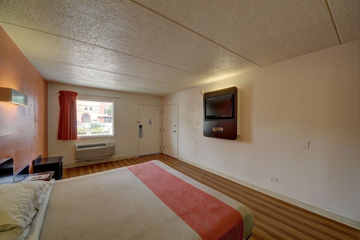 Une chambre d’hôtel avec un lit, un téléviseur fixé au mur, une fenêtre avec des rideaux et une porte.