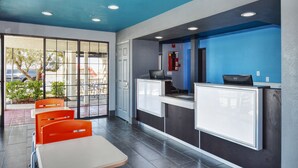 Un espace d’accueil avec un mur d’accent bleu, un bureau avec un ordinateur et un coin salon avec des chaises orange.