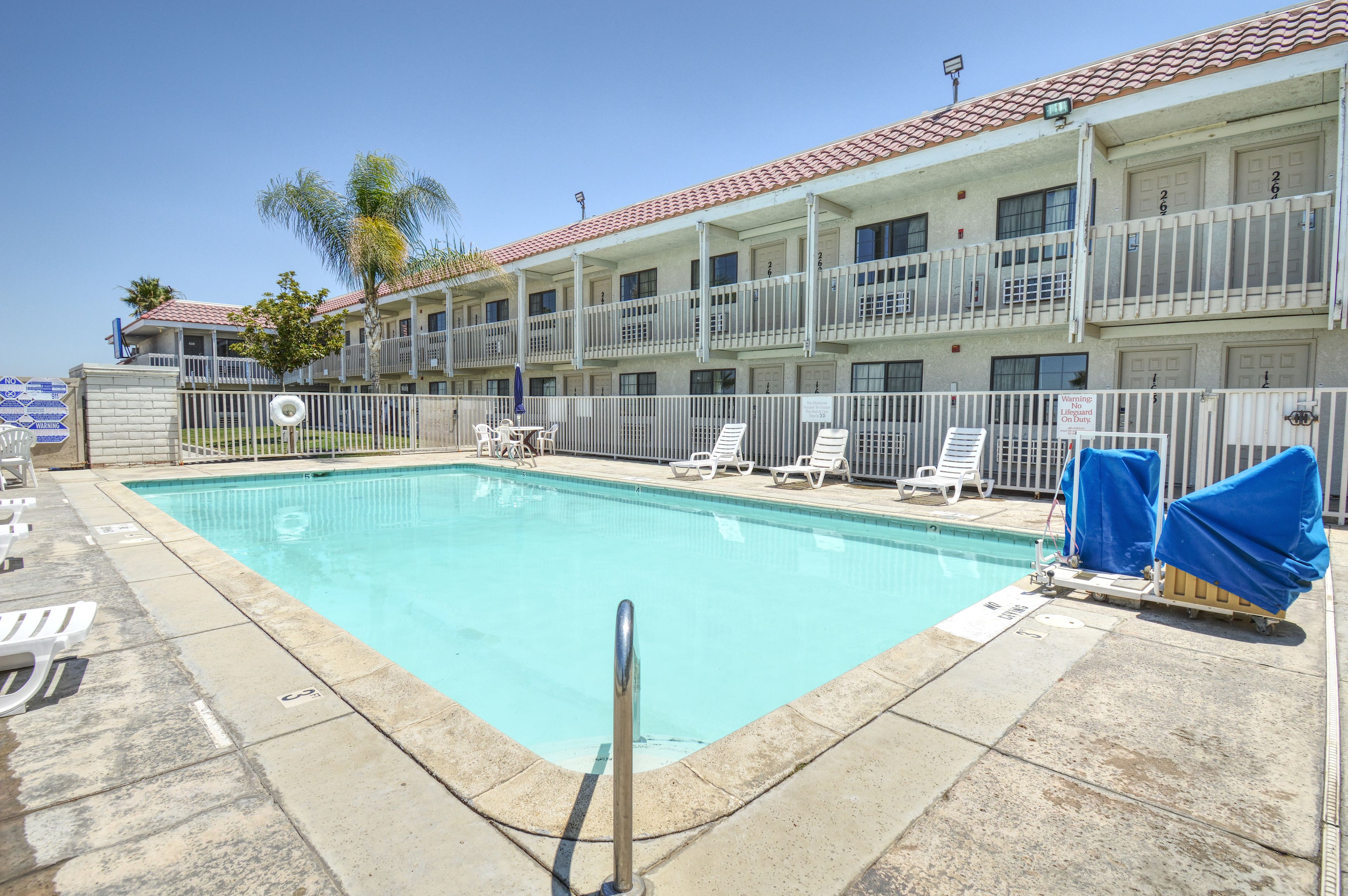A swimming pool with lounge chairs and a fenced area, surrounded by a multi-story building with balconies.