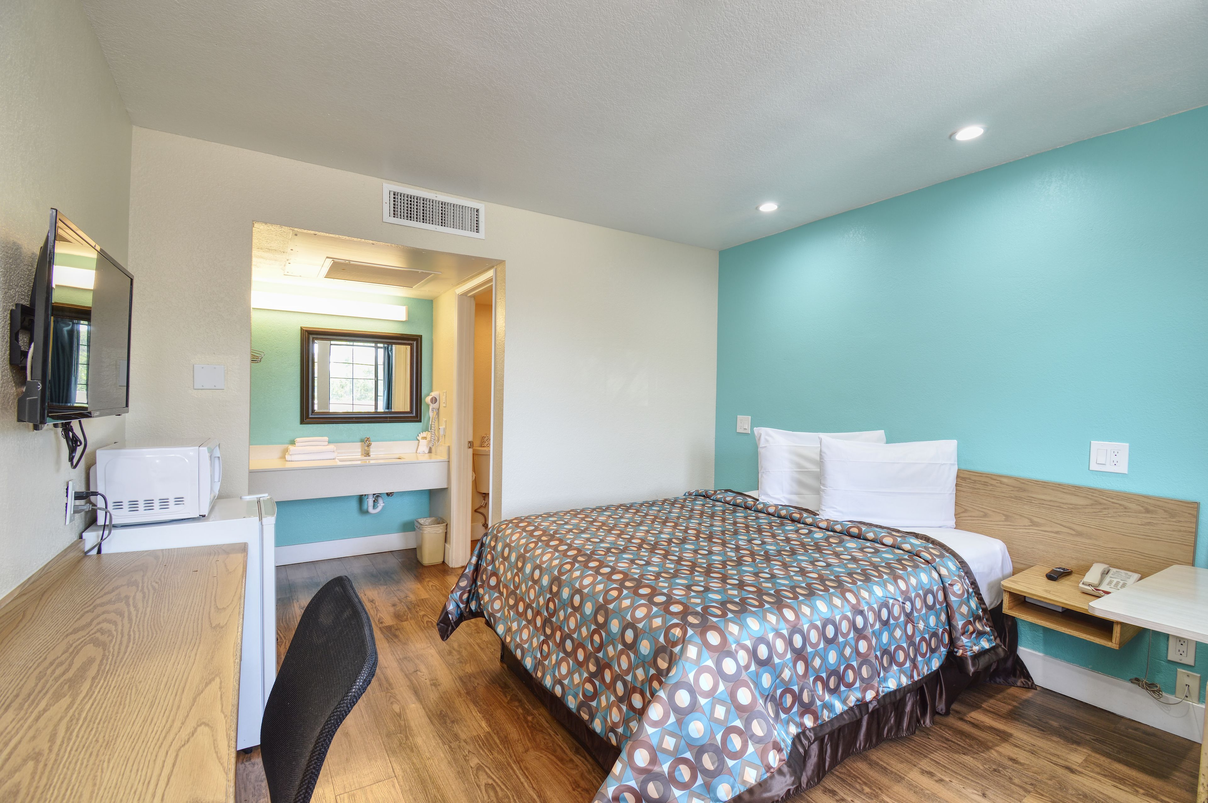 A hotel room with a bed, a desk, a chair, a mirror, a sink, and a window.
