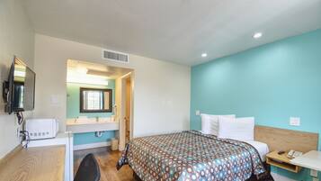 A hotel room with a bed, a desk, a chair, a mirror, a sink, and a window.