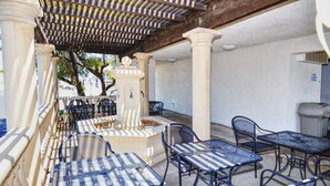 Une terrasse extérieure avec des tables et des chaises en métal, une fontaine décorative et une pergola au-dessus.