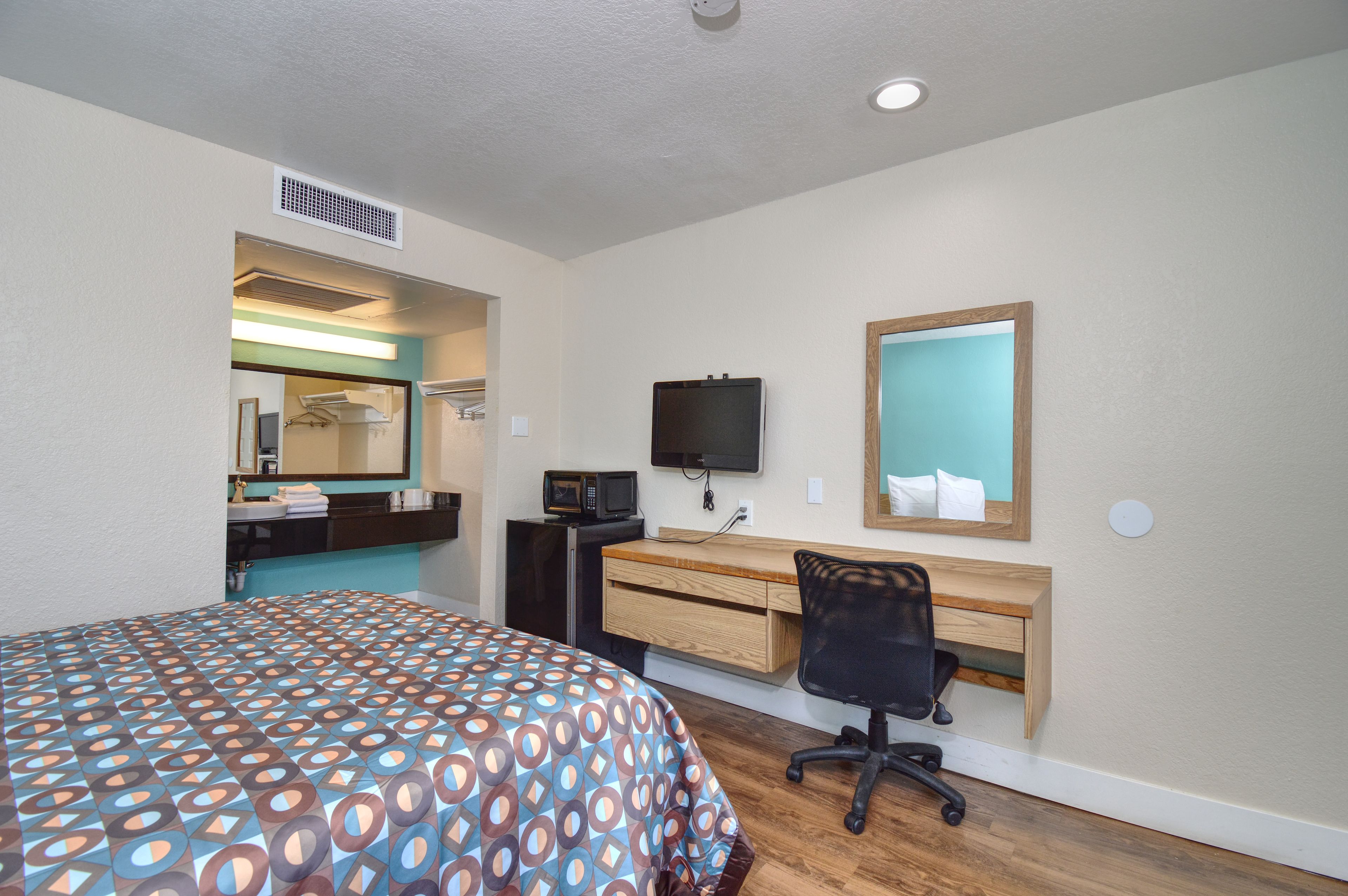 A hotel room with a bed, a desk with a chair, a television, and a mirror.