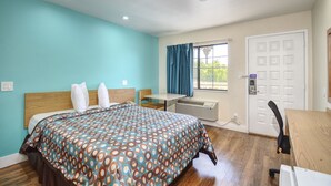 Une chambre d’hôtel comprenant un lit, un bureau, une chaise, une fenêtre avec des rideaux, un appareil de climatisation et une porte.