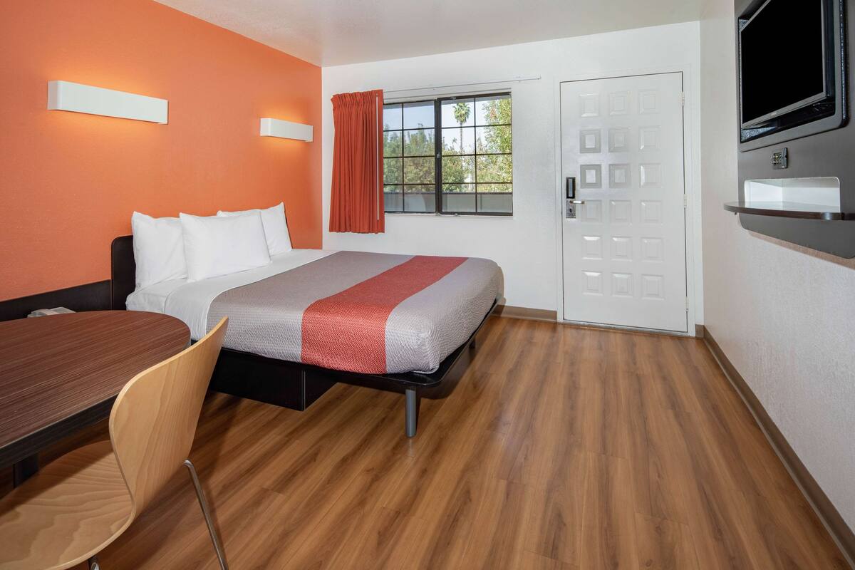 Une chambre d’hôtel équipée d’un lit, d’un bureau, d’une chaise, d’une télévision et d’une fenêtre avec des rideaux.