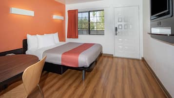 Habitación de hotel con cama, escritorio, silla, televisor y ventana con cortinas.