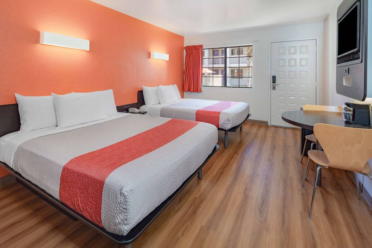 Une chambre d’hôtel avec deux lits, une télévision, un bureau et une fenêtre avec des rideaux.