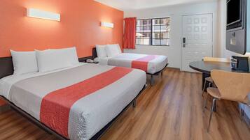 A hotel room with two beds, a TV, a desk, and a window with curtains.