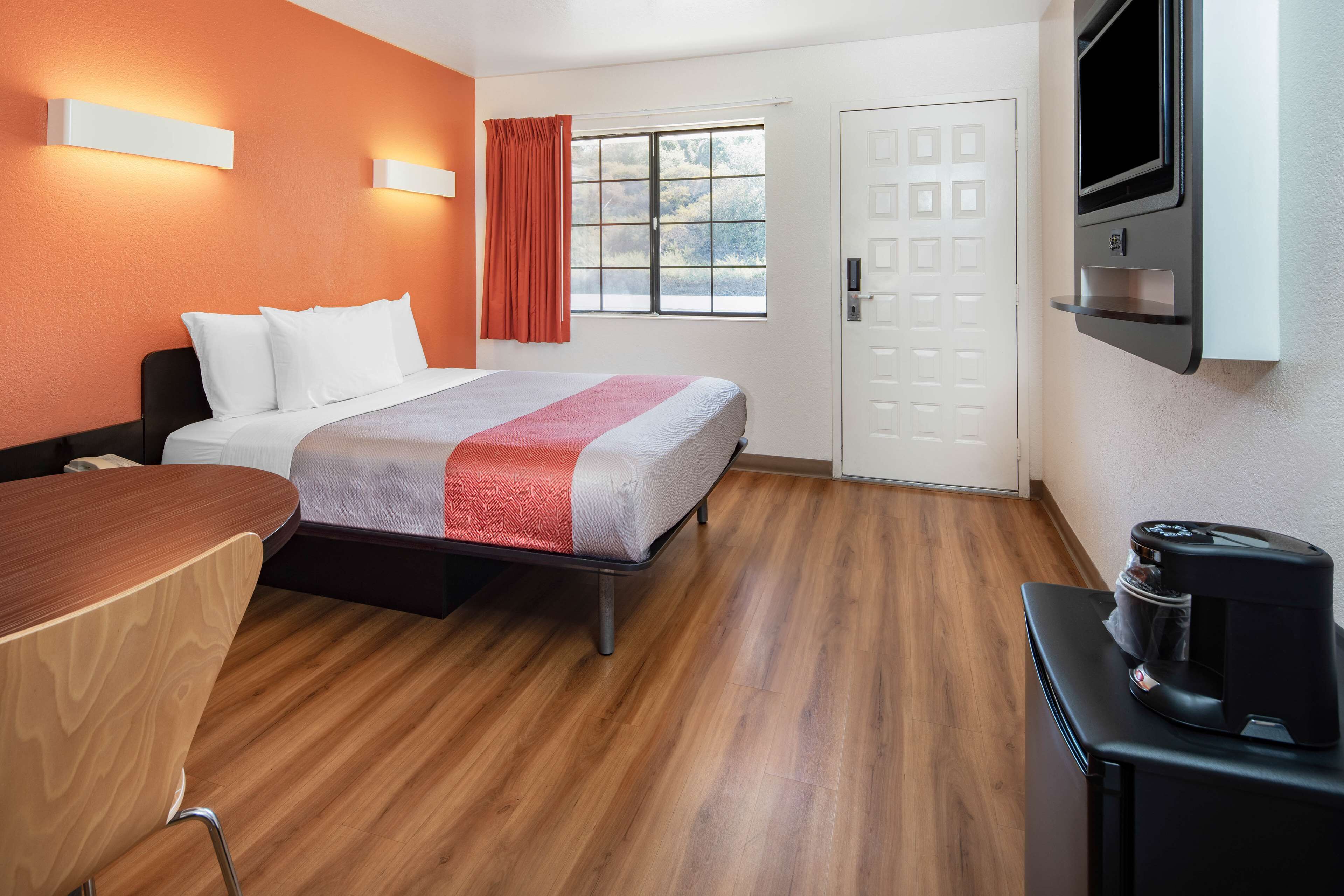 A hotel room with a bed, a desk, a coffee machine, and a TV mounted on the wall.