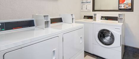 A laundry area with two washing machines and two dryers, a wall-mounted air conditioner, and a mirror with a poster.