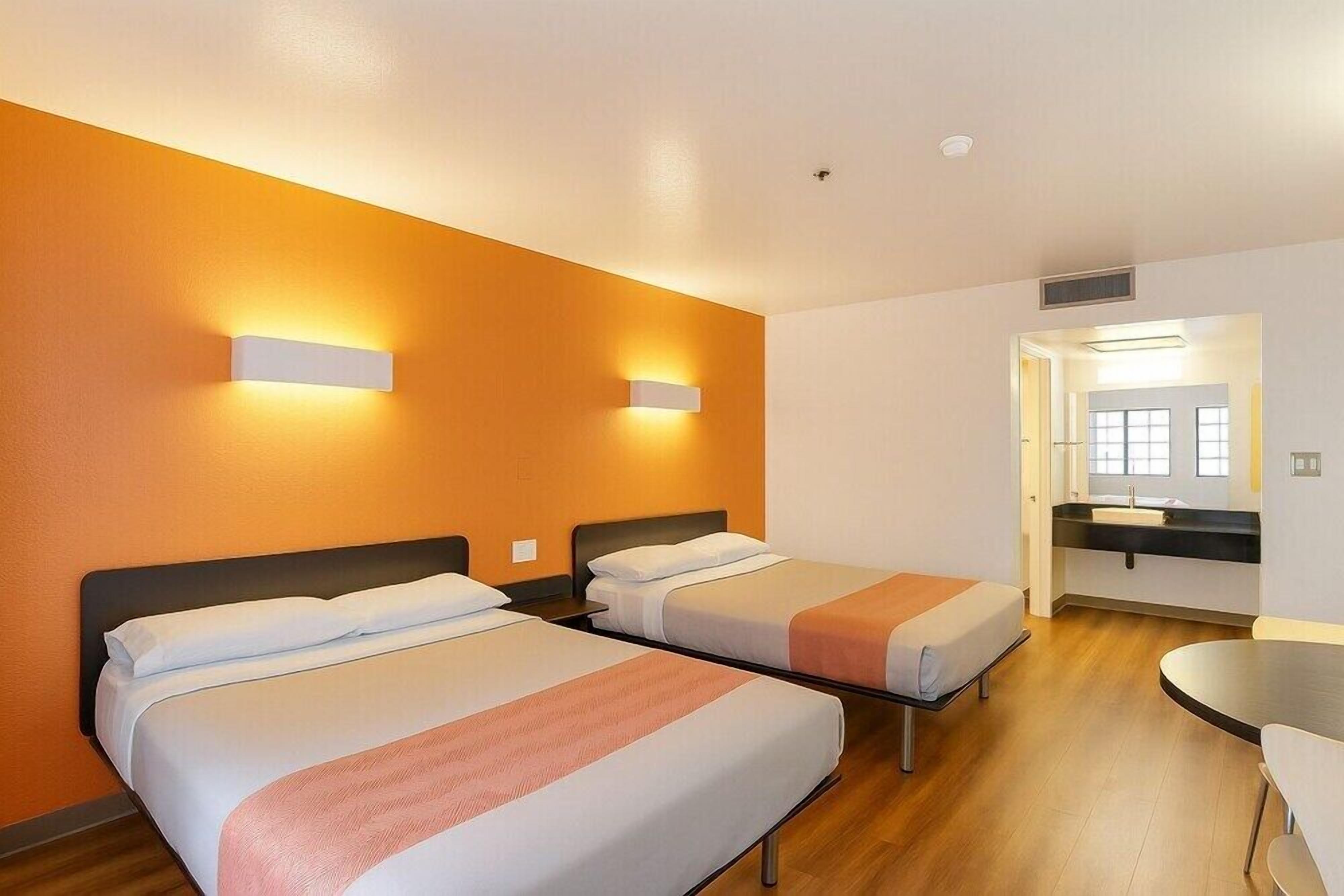 Habitación de hotel con dos camas, una mesita y un baño visible a través de una puerta abierta.