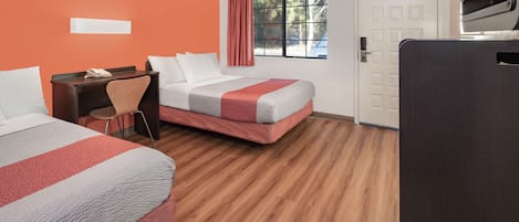 Habitación de hotel con dos camas, un escritorio, una silla, un televisor y una ventana con cortinas.