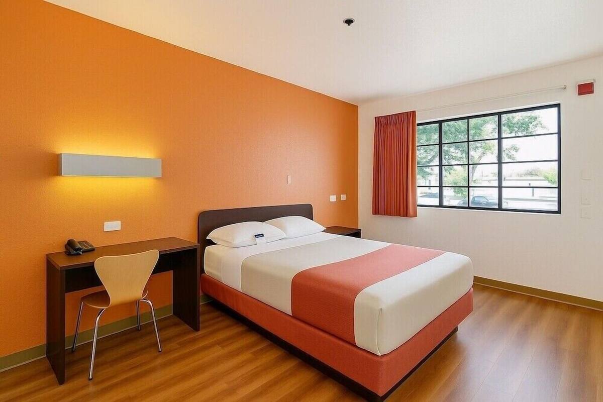 Une chambre d’hôtel avec un lit, un bureau, une chaise et une fenêtre avec des rideaux.