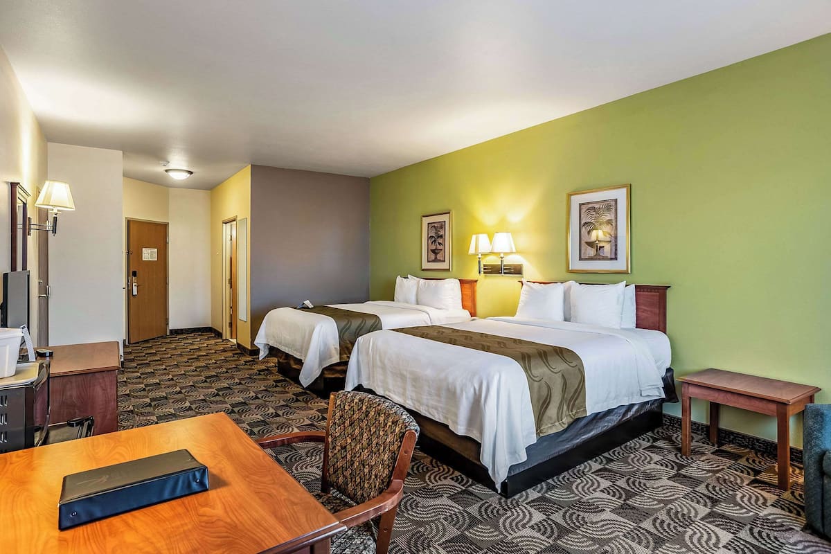 A hotel room with two beds, a desk, a chair, and a small table.