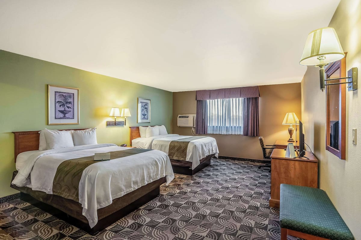 A hotel room with two beds, a desk, a chair, a bench, and a patterned floor.